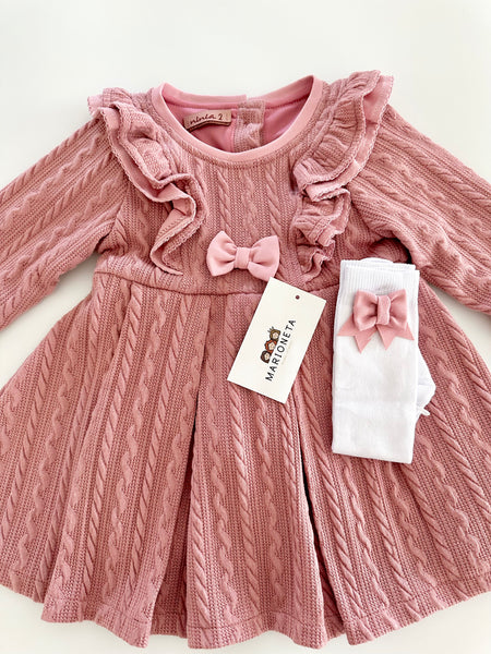 Vestido color rosita con olanes y medias blancas con adorno de lazos para niña.