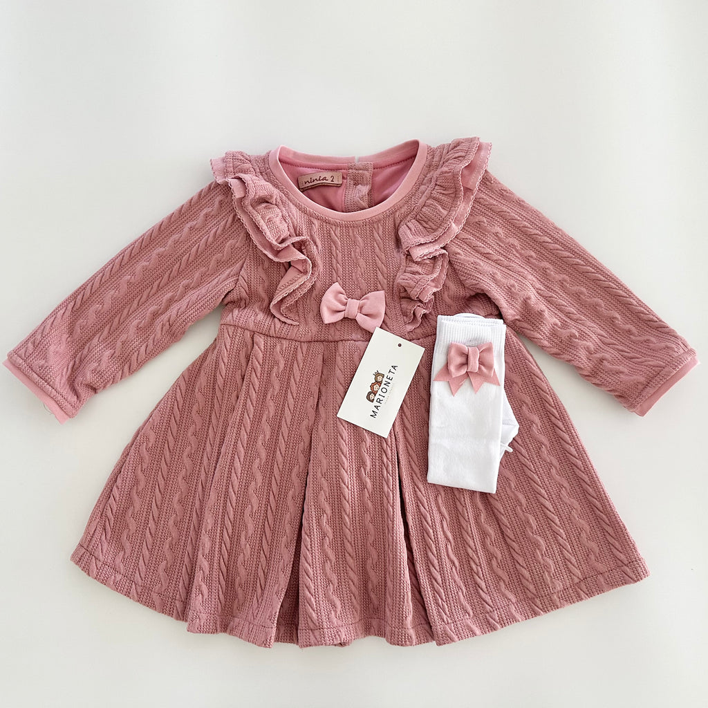 Vestido color rosita con olanes y medias blancas con adorno de lazos para niña.