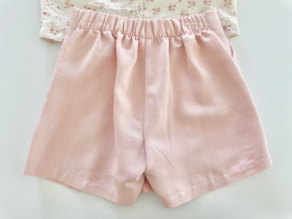 Conjunto dos piezas blusa ivory con detalle de moños al frente y falda short color rosa para niña.