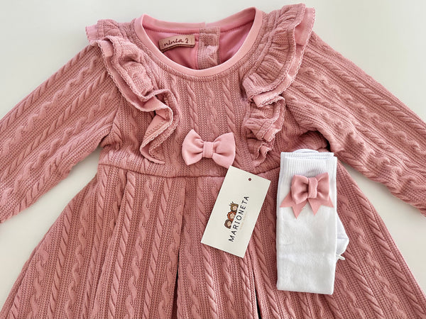 Vestido color rosita con olanes y medias blancas con adorno de lazos para niña.